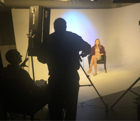 Photographers inside a studio taking a photo of a female sitting cross-legged in front